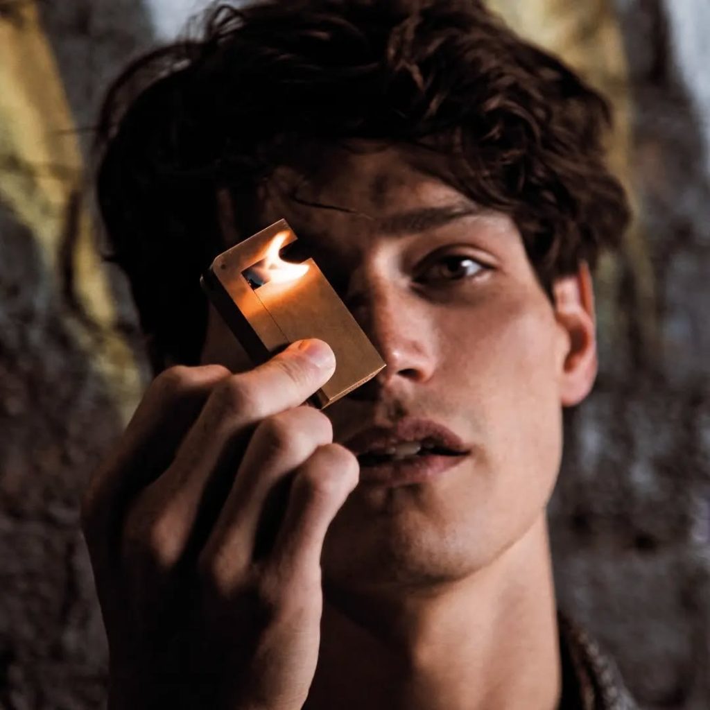 Young man lighting a KNNOX brass lighter near his face